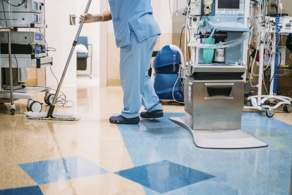 Cleaner mopping hospital floor near medical equipment.