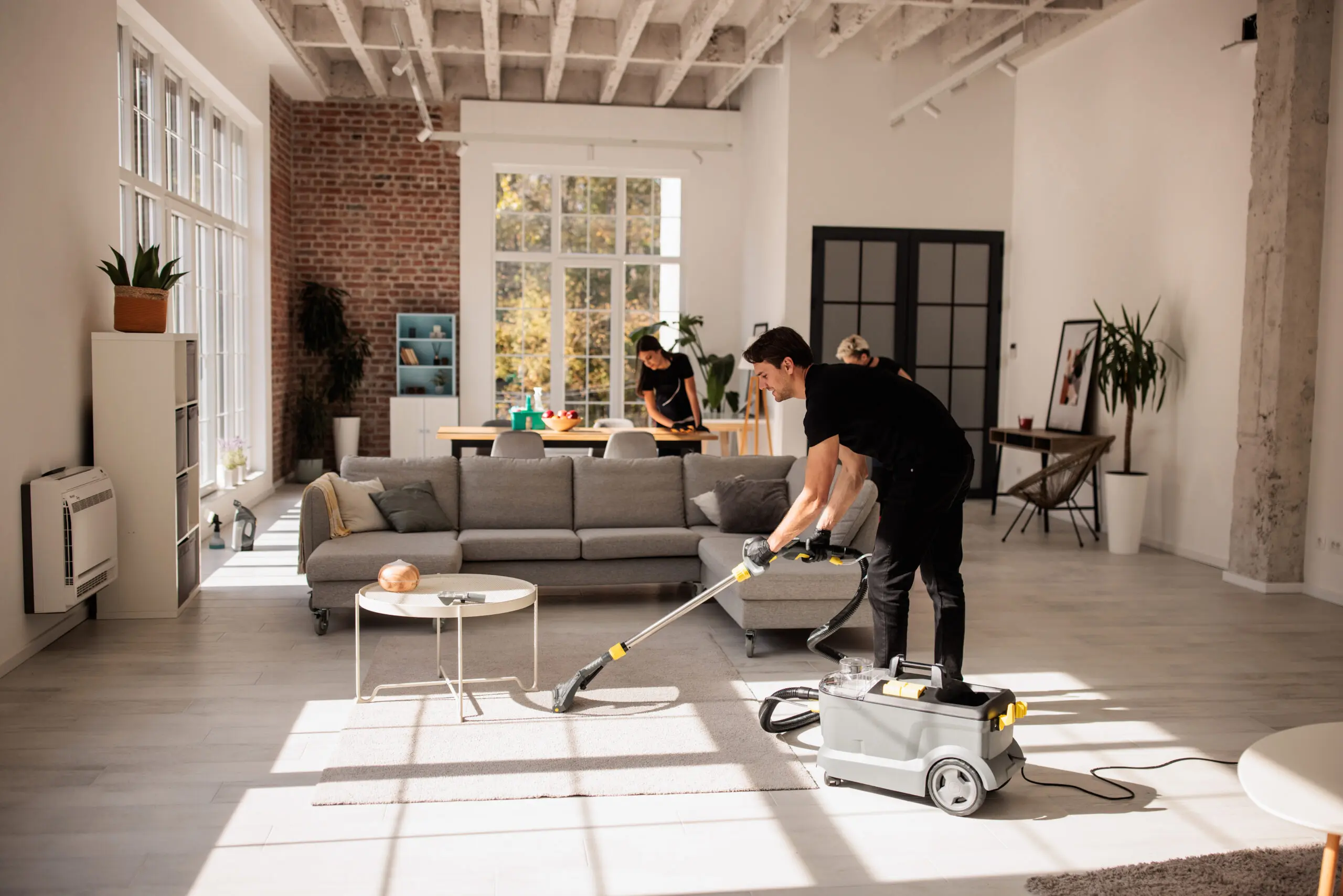 Group of experienced cleaners collaborating to deep clean a spacious apartment. Male worker is vacuuming the carpet.