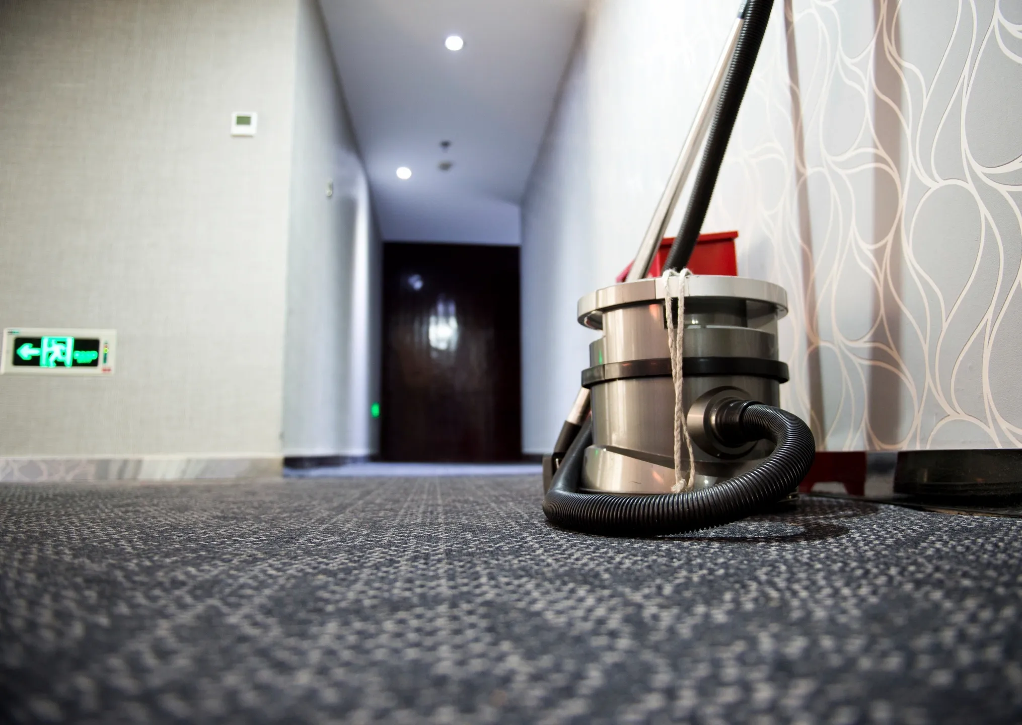 Vacuum cleaner left on carpeted hallway floor.
