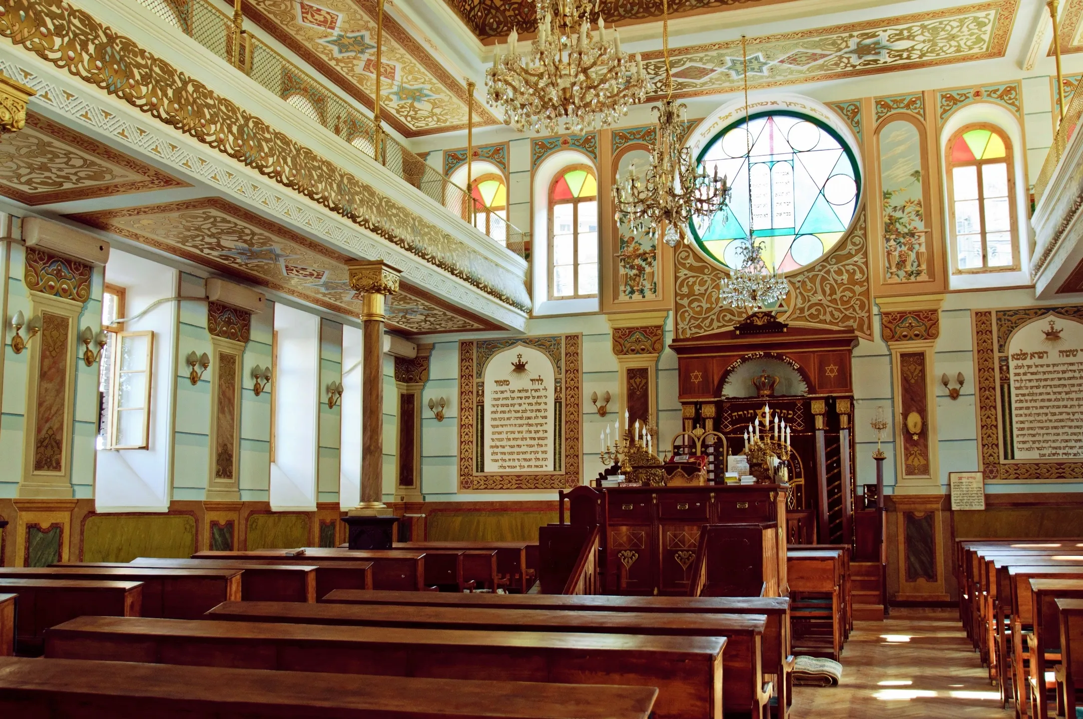 Interior of an ornate synagogue with wooden pews and stained glass windows.